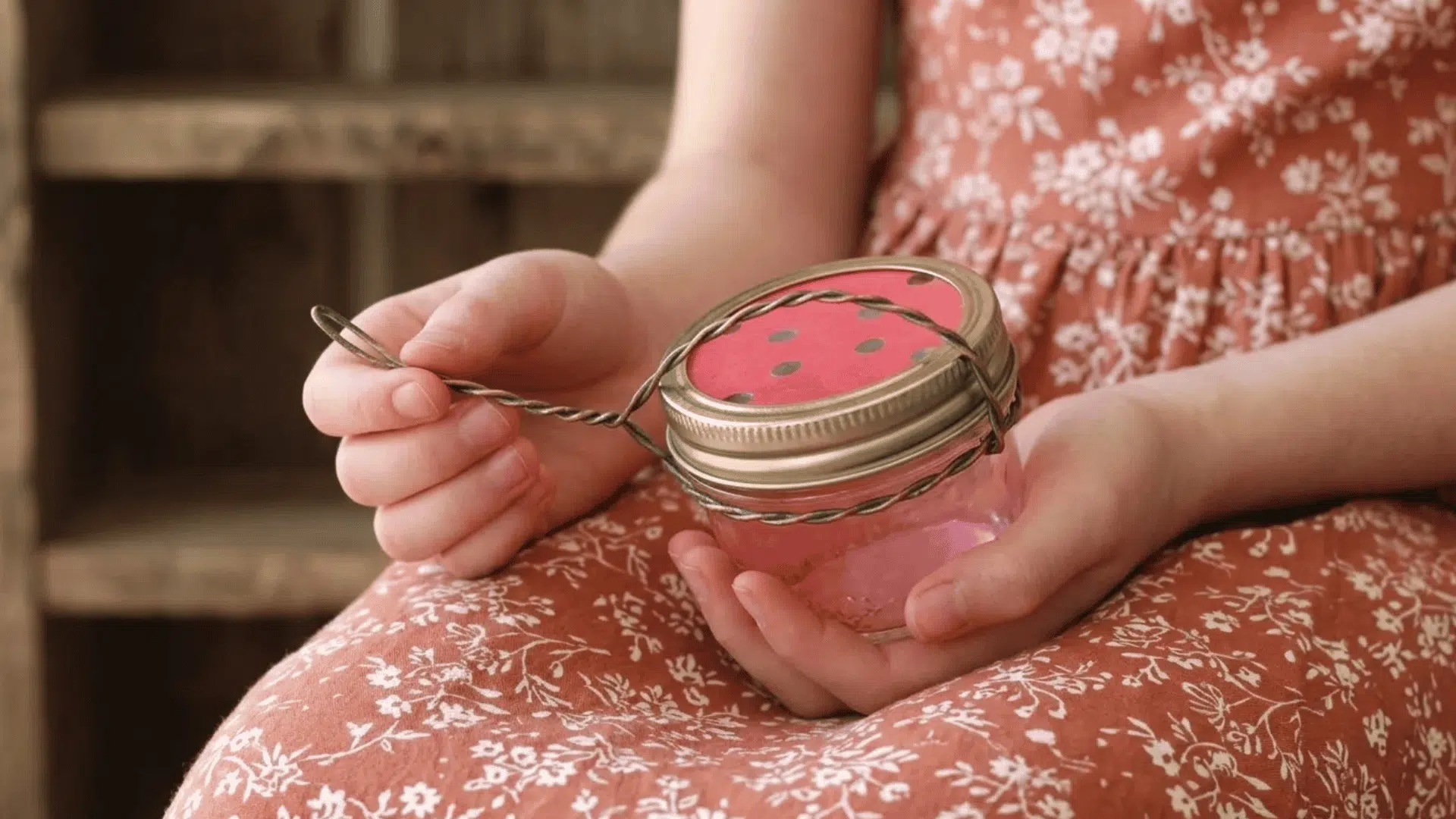 Child holding a small mason jar hummingbird feeder with a red lid and wire handle