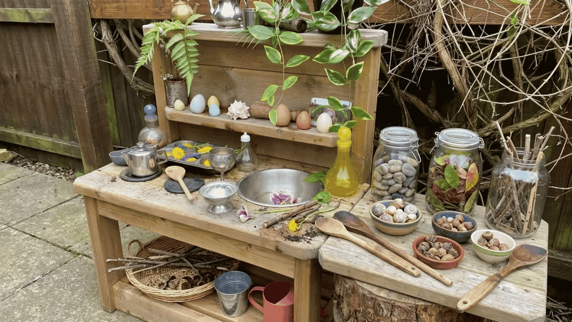 Forest potion station mud kitchen with natural materials, jars, flowers, sticks, stones, and a built-in mixing area for imaginative outdoor play.