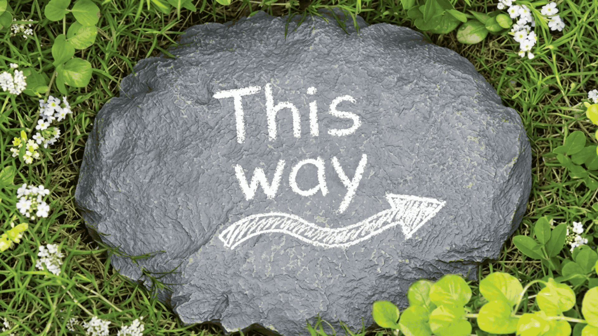 Gray letter stamp stepping stone with white “This way” text and arrow in grass.