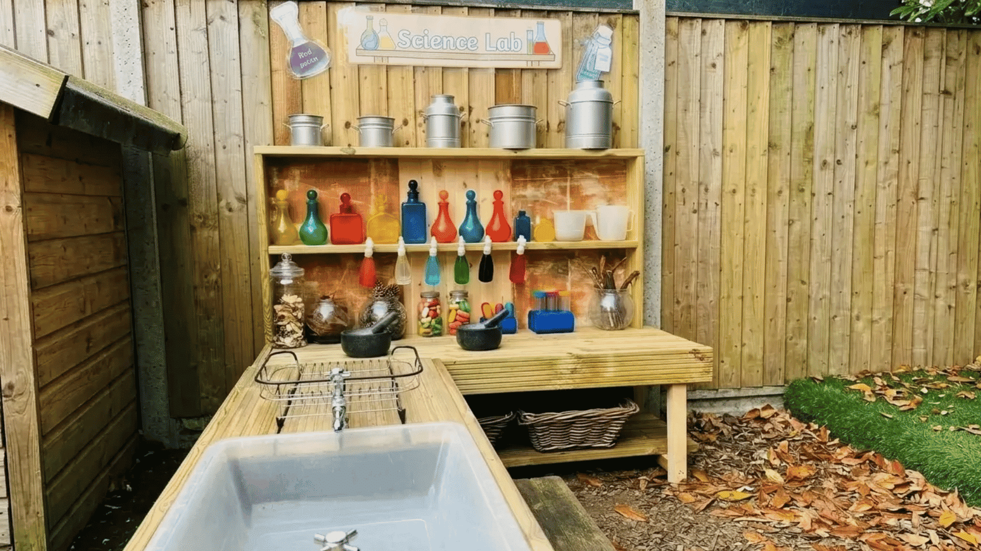 Outdoor science lab mud kitchen with experiment bottles, a sink station, shelves, and hands-on tools for outdoor play.
