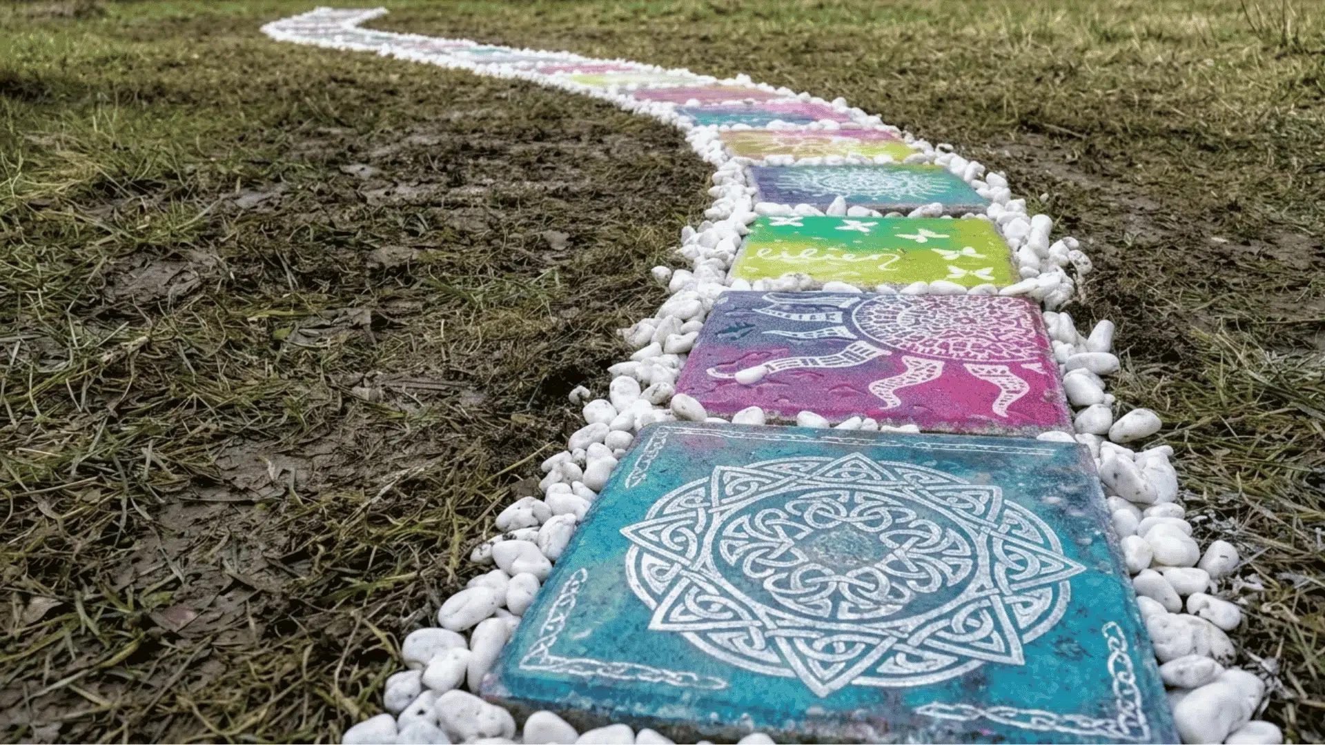 Painted colorful square stepping stones with white pebble borders forming a winding outdoor path.