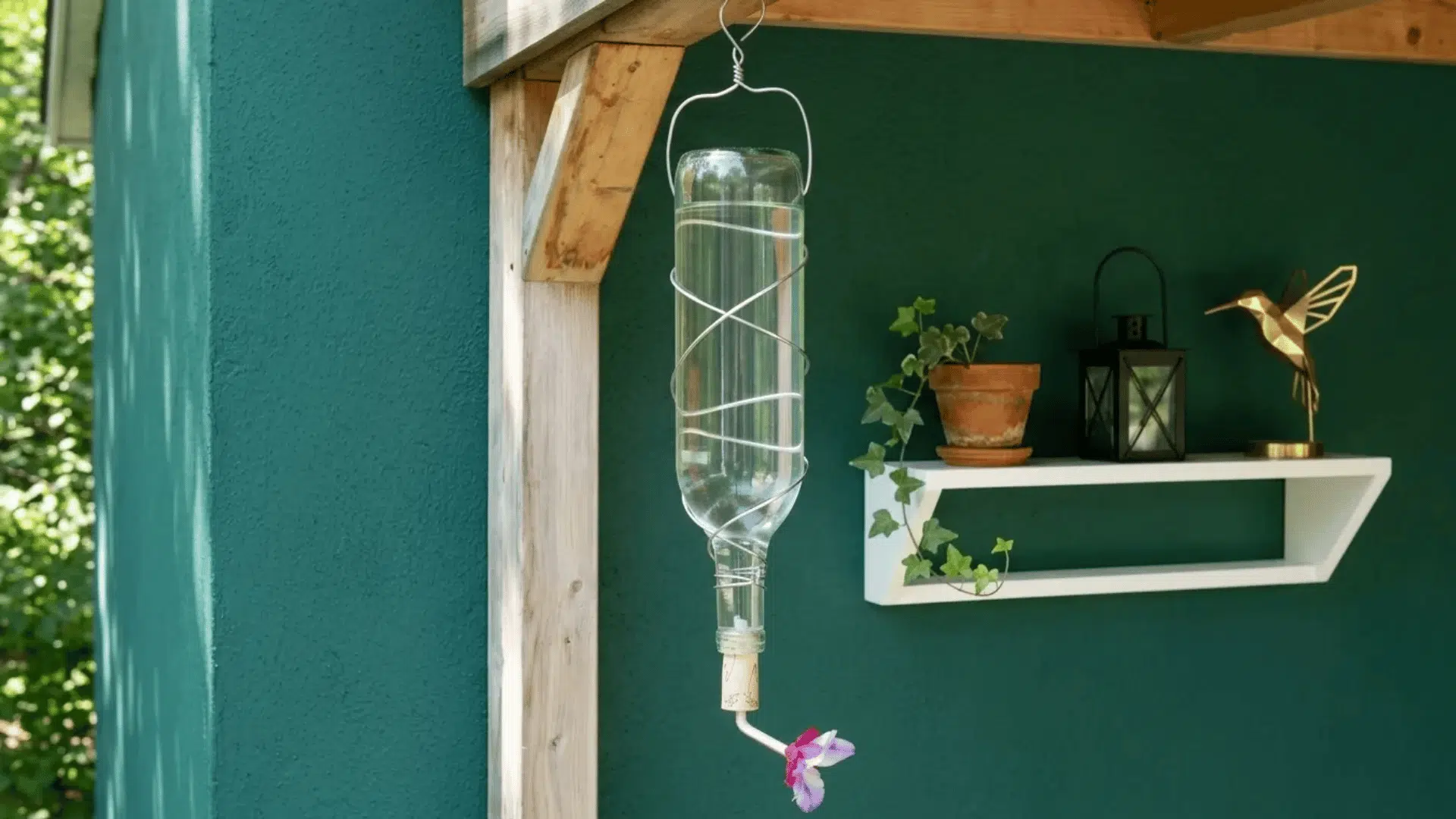 Recycled bottle hummingbird feeder hanging from a porch with wire wrap and a small flower feeding tube