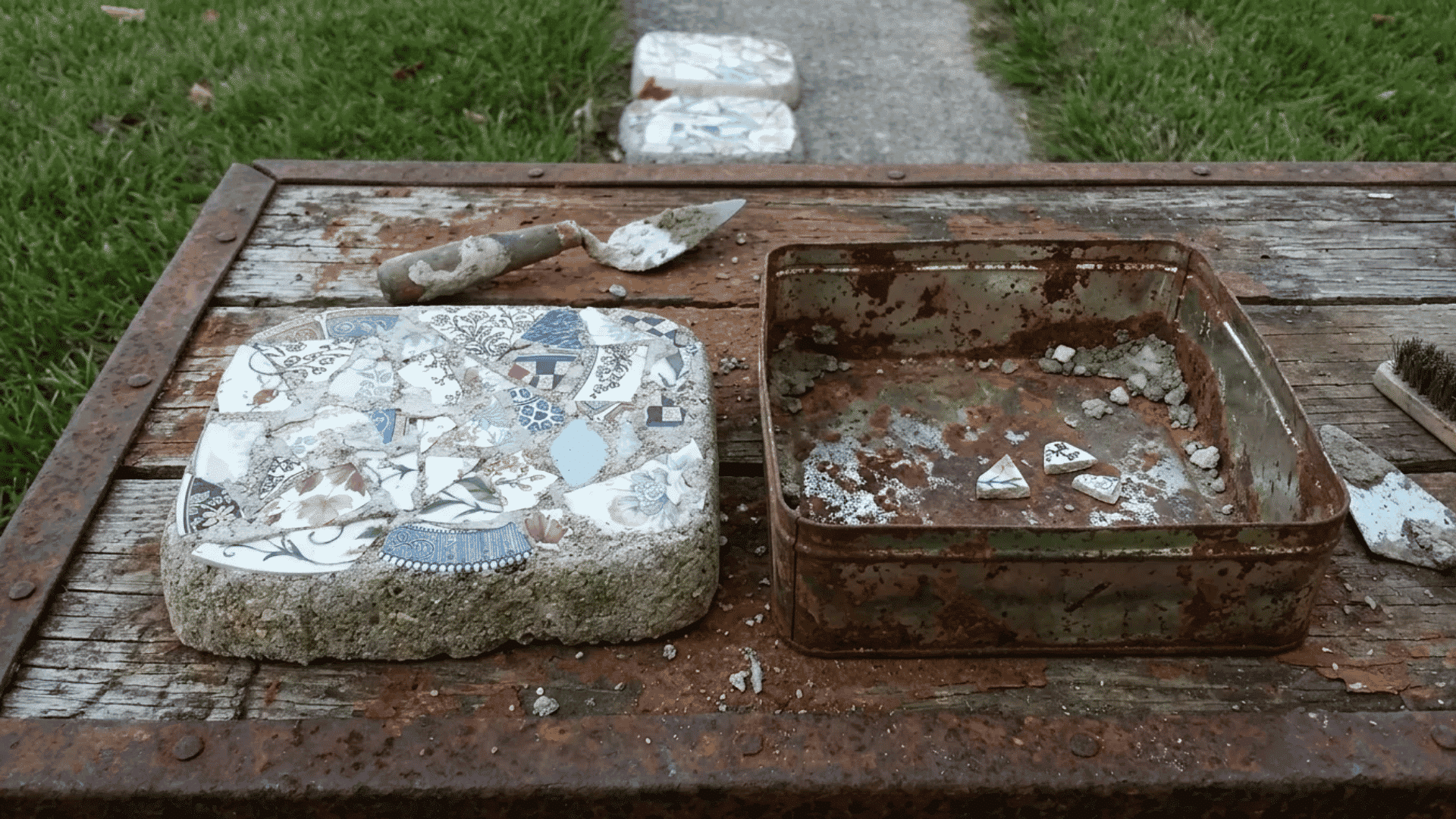 Recycled mold stepping stone with broken tile pieces beside an old metal pan and trowel.