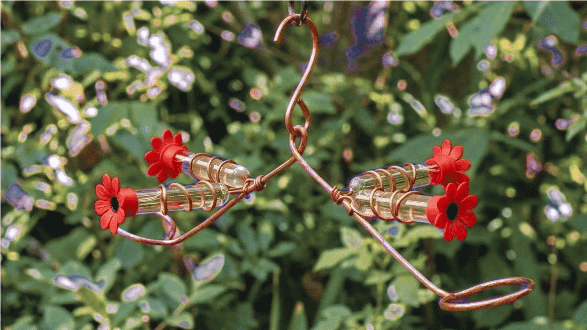 Test tube DIY hummingbird feeder with red flower tips and copper wire hanging in a garden