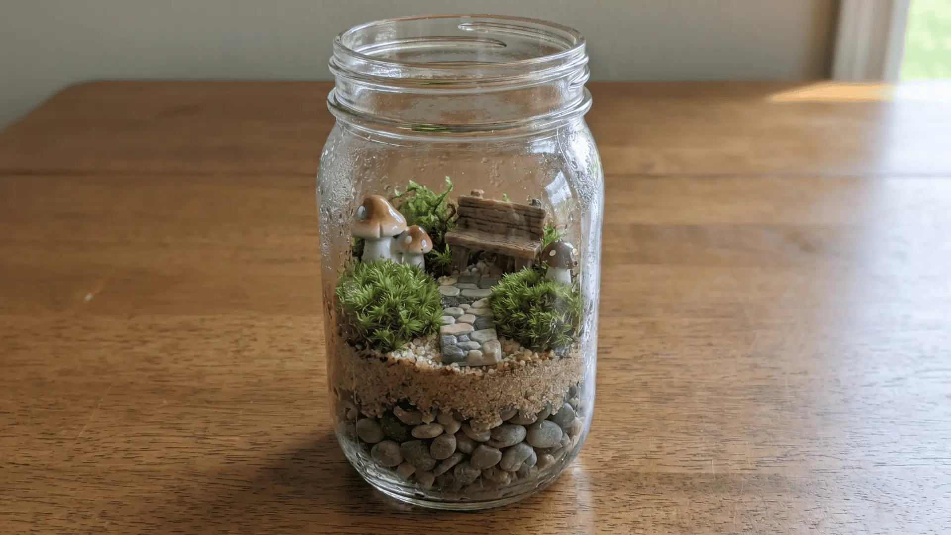 Open mason jar with pebbles, sand, moss, and tiny garden pieces