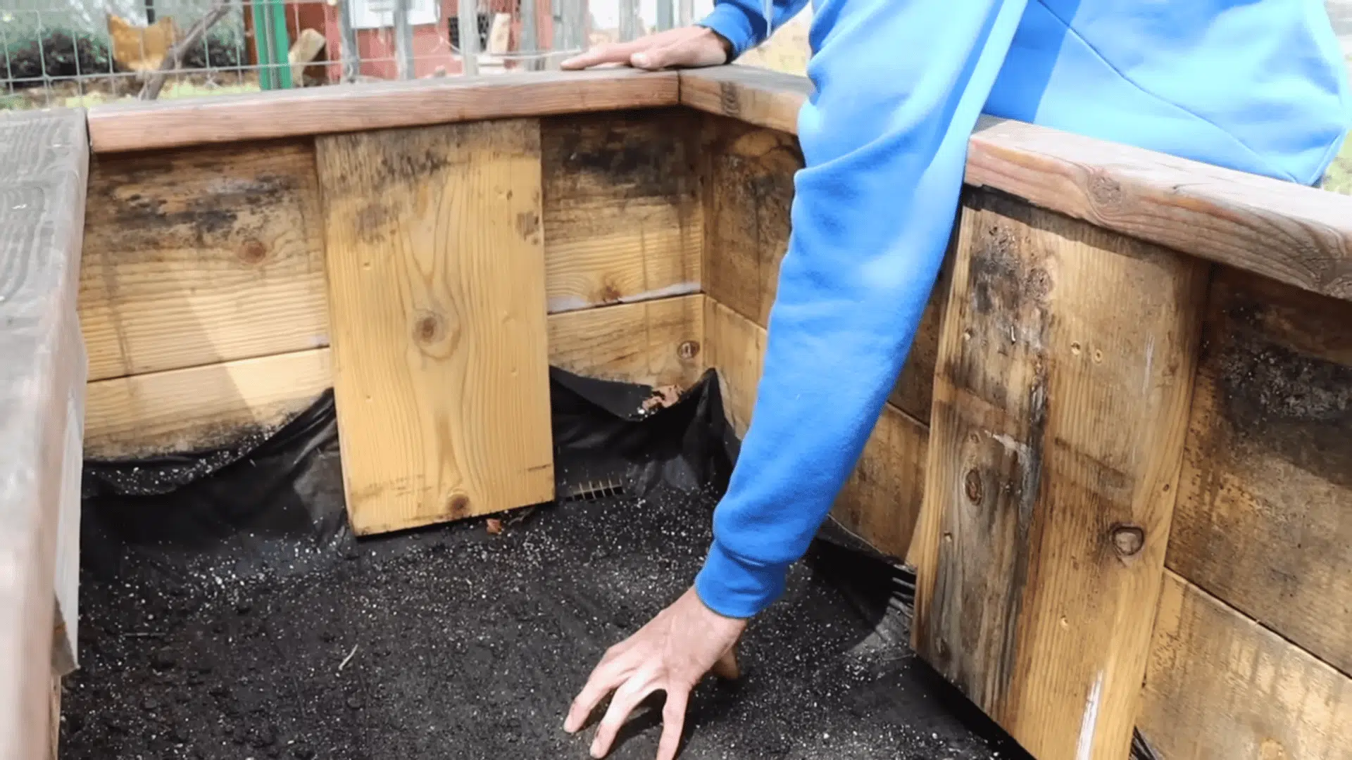 person lining the empty bottom of a wooden planter demonstrating how to fill raised garden beds