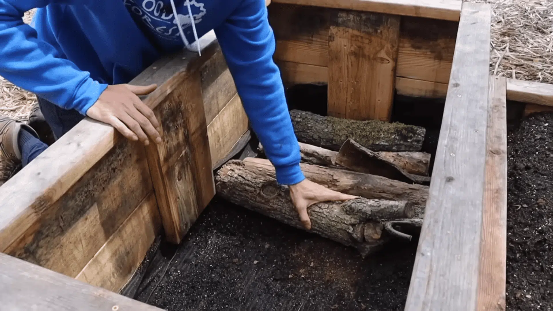 placing large logs at the bottom of a wooden planter showing how to fill raised garden beds