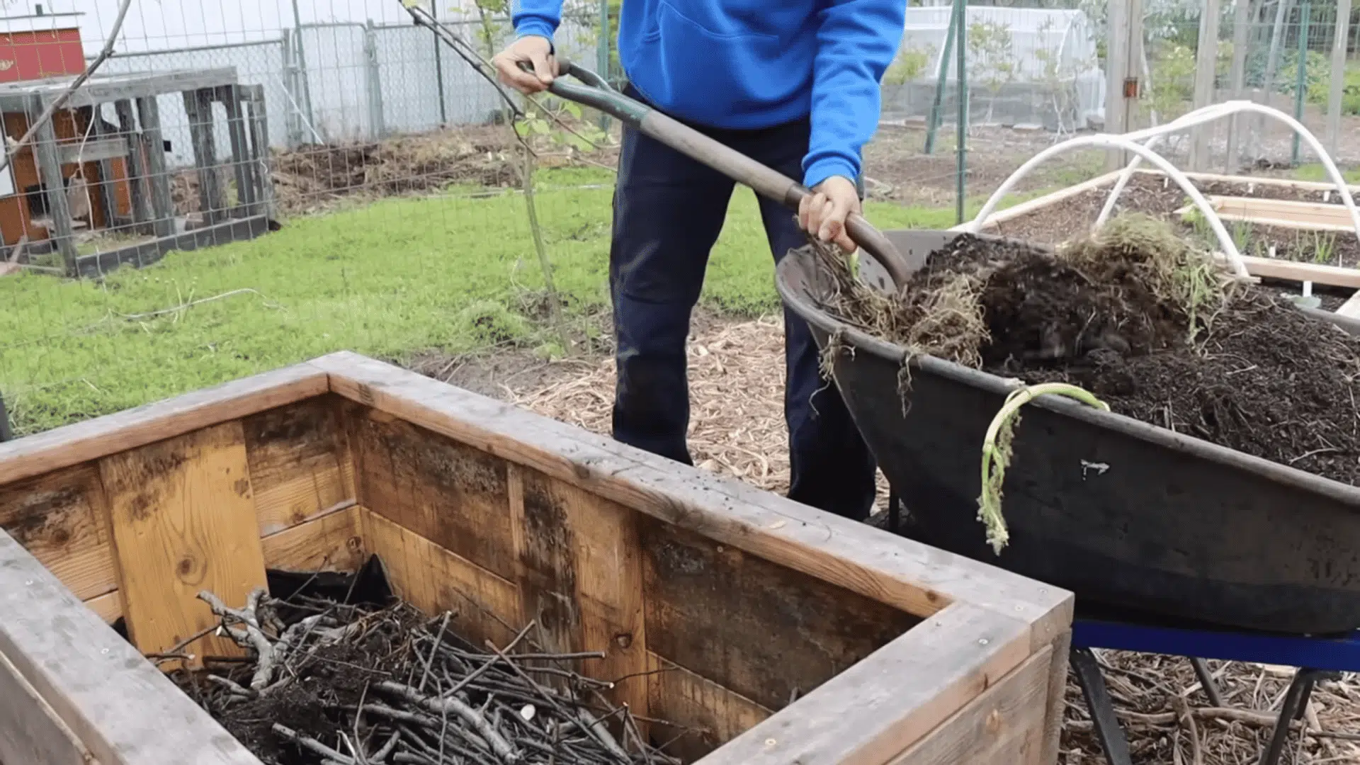 shoveling compost and small branches into a planter to show how to fill raised garden beds