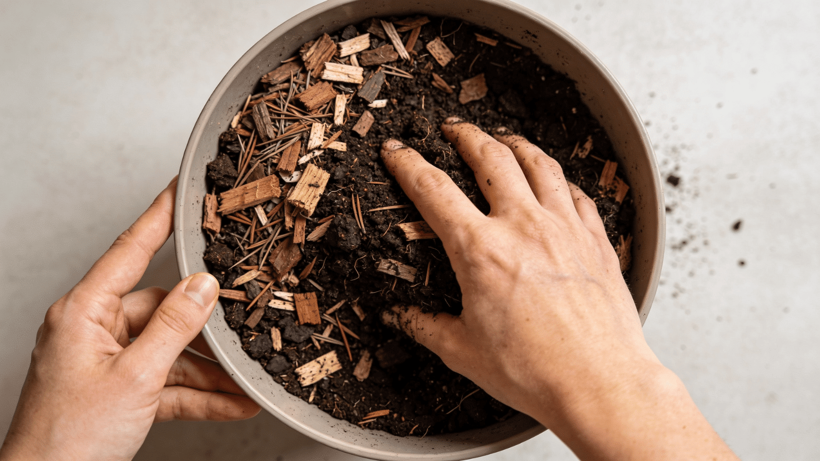 Hands mixing peat, pine bark, and compost into a potting mix