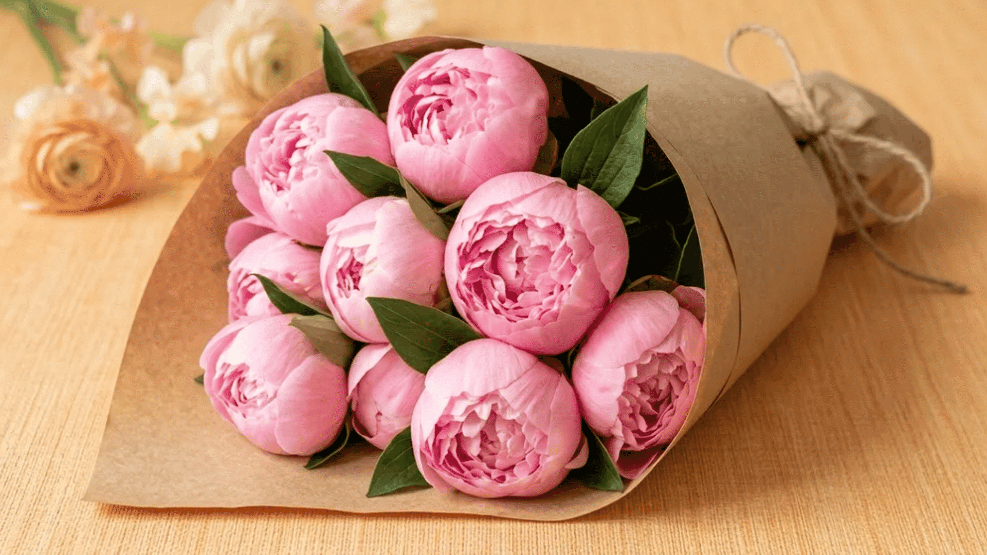 Bouquet of soft pink peonies wrapped in brown paper resting on a wooden surface, symbolizing flowers that represent healing and gentle comfort.